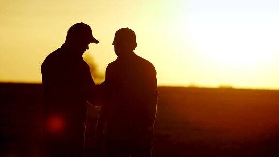 经营农业两个男农民在田间交流用药片握手轮廓在日落时分