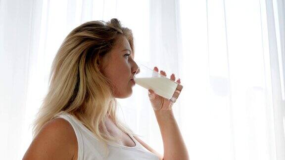 身为母亲美丽的孕妇喝着杯子里的牛奶揉着肚子