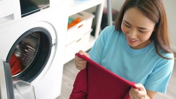 亚洲美丽的女人拿出和闻到新鲜的衣服从洗衣机在家里家庭