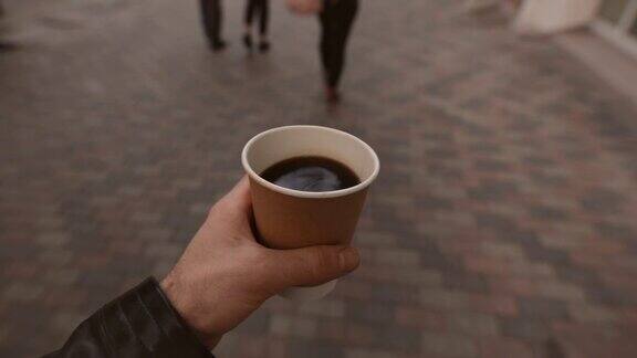 POV一个拿着咖啡杯走在城市街道上的男人