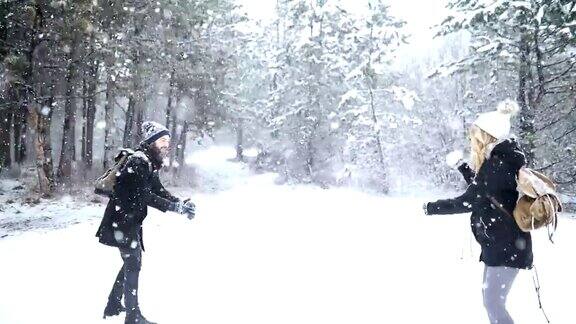 无忧无虑的快乐的年轻夫妇一起在雪地里玩在冬天的林地里互相扔雪球在一个模拟战斗
