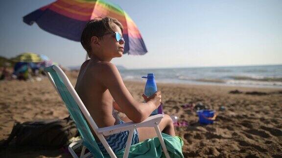 沙滩上的小男孩用可重复使用的水瓶喝水