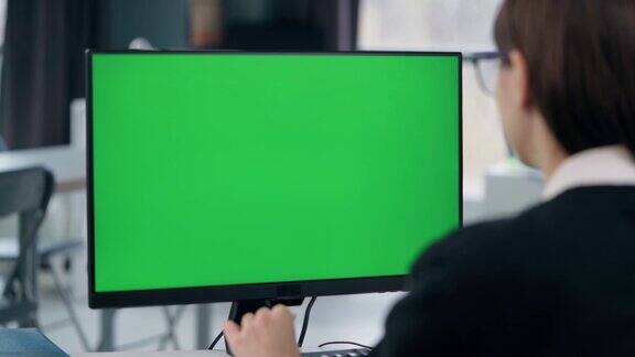 年轻的女孩在办公室用绿色的模拟屏幕在电脑前工作