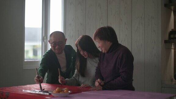 亚洲华人家庭在红纸上书写中国书法以求繁荣准备中国新年的家庭装饰