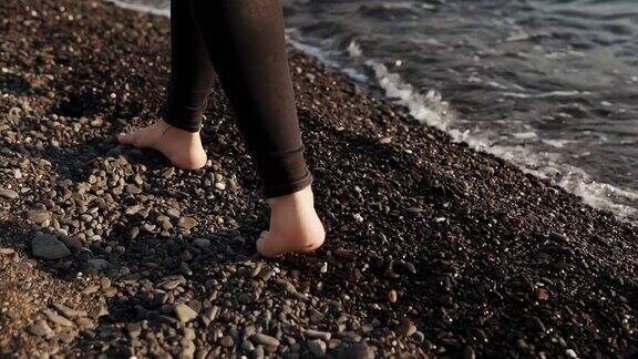 苗条的年轻女子光着脚走过海水附近的卵石滩