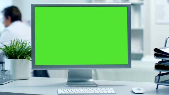 一个绿色屏幕显示器的特写医生在他的办公桌后面工作在一个现代医疗办公室拍摄的