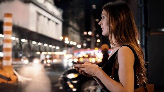 在美国纽约年轻漂亮的女人晚上站在市中心用着智能手机