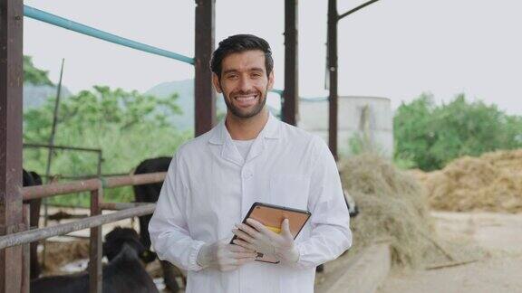 英俊的男兽医在牛棚户外工作的肖像正在检查奶牛的年轻专业医生一边走在畜牧场一边看着摄像机一边检查奶牛并做记录