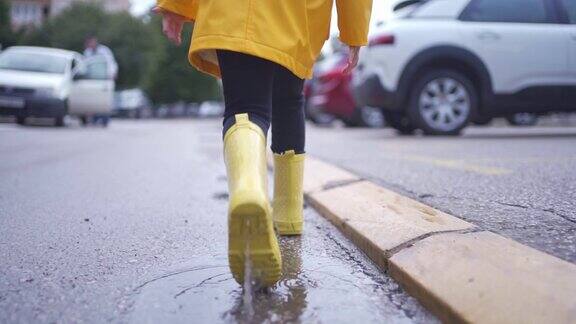 穿着黄色橡胶靴子的孩子在室外城市街道的水坑里泼水