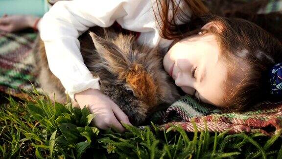 小女孩和棕兔躺在绿色的草坪上拥抱着女孩和心爱的宠物玩耍Linography兔子