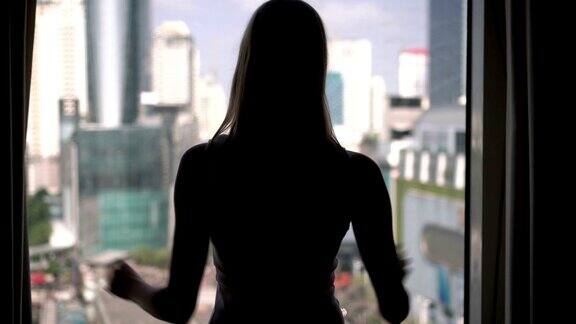 女人揭开窗帘向窗外望去的剪影城市摩天大楼景观