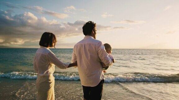 日落时分快乐的父母带着宝宝在海滩上散步