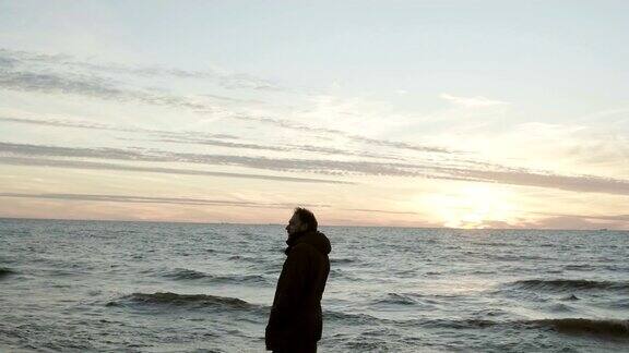 一个年轻英俊的男子站在海边看着夕阳男性在享受海滩上的风景