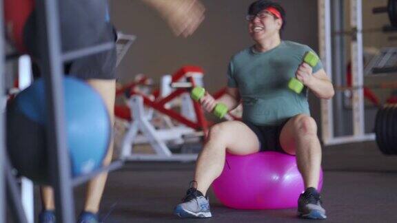 亚洲肥胖男性正在健身馆里用健身球上的哑铃努力工作喜剧演员