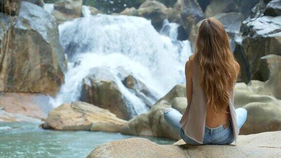 金发女孩坐在瀑布附近的石头上