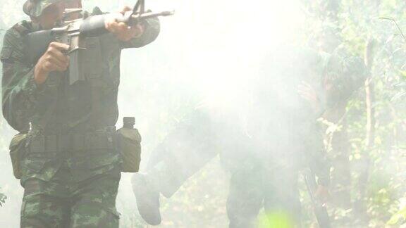 手持枪械的士兵穿着带烟雾的装甲制服士兵们正把受伤的人抬出丛林