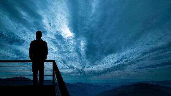 那个男人站在阳台上在夜山的背景上hyperlapse