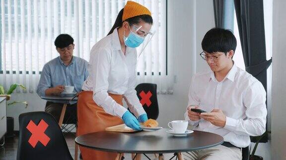 亚洲员工餐厅服务员在餐厅工作时佩戴防护口罩社交距离保护感染新冠病毒