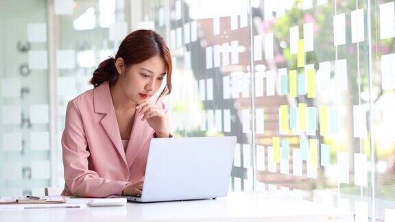 有魅力的亚洲女商人在办公室用笔记本电脑工作时思考