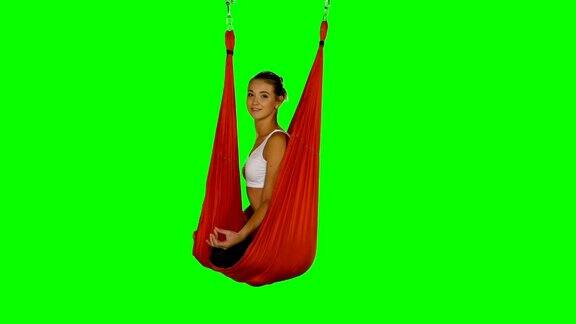年轻女子在红色吊床上做反重力瑜伽练习