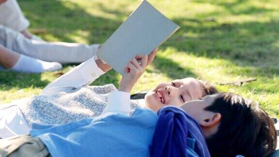 亚洲小女孩和小男孩躺在草地上看书