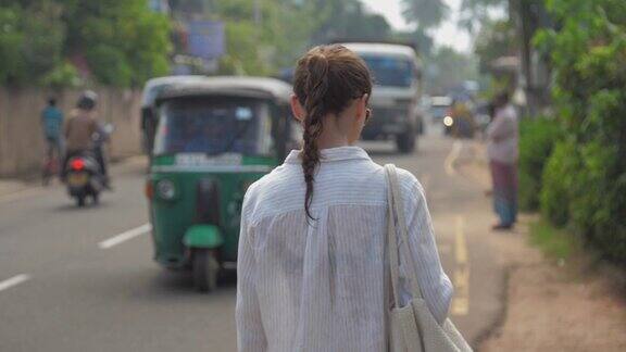 女孩走在热带城市的道路上经过移动的车辆