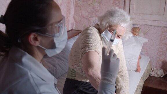 隔离期间的冠状病毒防护女医生在家中给一位老年妇女接种疫苗