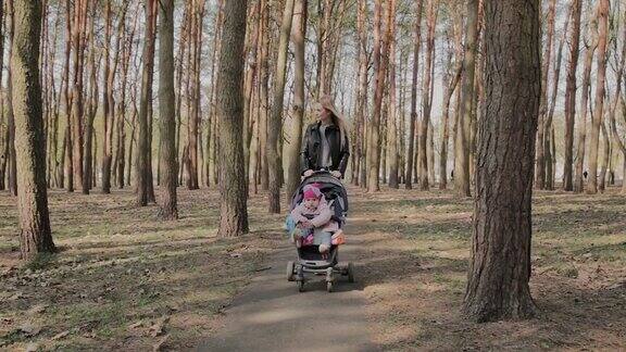 美丽的女人在公园里推着婴儿车和她的小女儿散步妈妈推着婴儿车在公园里散步