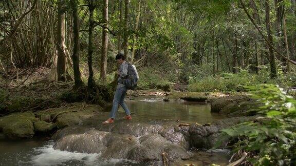 夏日旅行中女背包客走在小溪上驻足观赏热带森林的美景