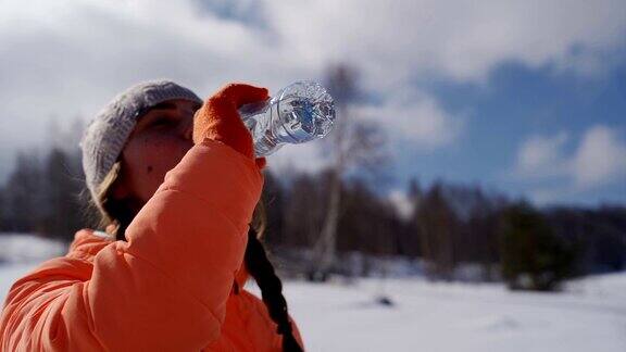 年轻美丽的女孩在山上喝着塑料瓶里的水