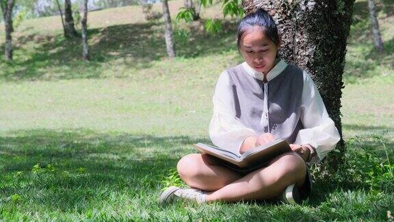 亚洲妇女坐在树下看书在公园