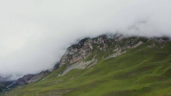 山谷中有绿色的小山脚下的悬崖被云朵覆盖着