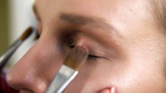 化妆师用两个专业的画笔给模特的眼睑涂上明亮的眼影关闭了构成的过程