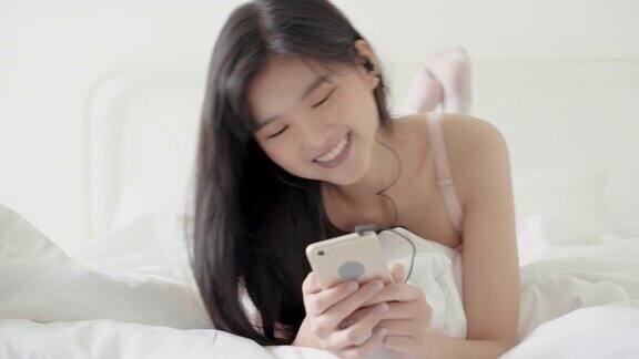 美丽年轻的亚洲女人躺在幸福的耳机听音乐与放松和享受在卧室女孩的乐趣和放松耳机与播放歌曲mp3智能手机上生活理念