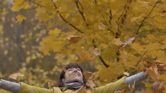 快乐的女人把秋天的黄叶抛起来落叶落在女人身上