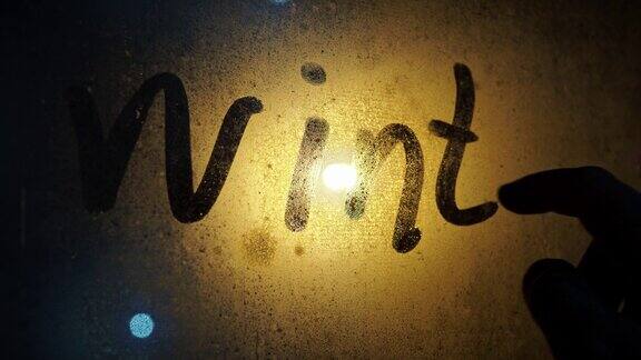 一个男人的手在雾蒙蒙的玻璃上写下了铭文冬天窗外的雪在一盏点着的灯笼的光下特克斯在窗户上