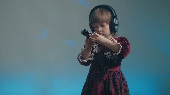 小女孩戴着大耳机穿着复古的裙子在手机上听音乐