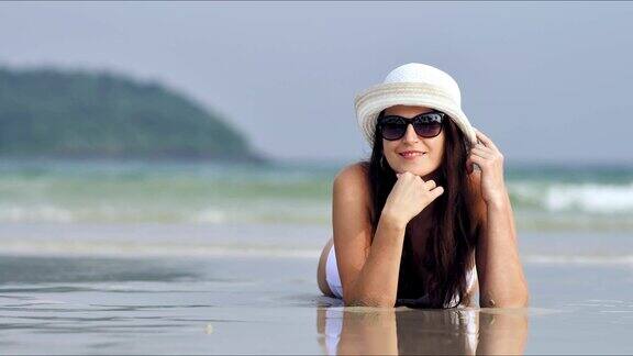年轻漂亮的女人在太阳眼镜放松和日光浴在热带海滩