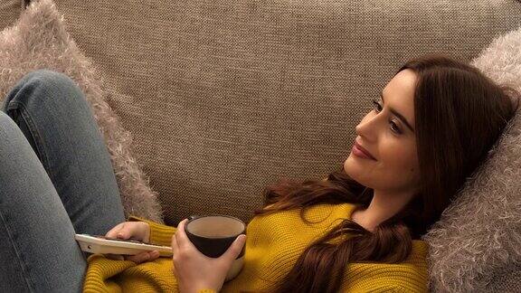 看电视换频道年轻女子躺在沙发上手里拿着一个咖啡杯