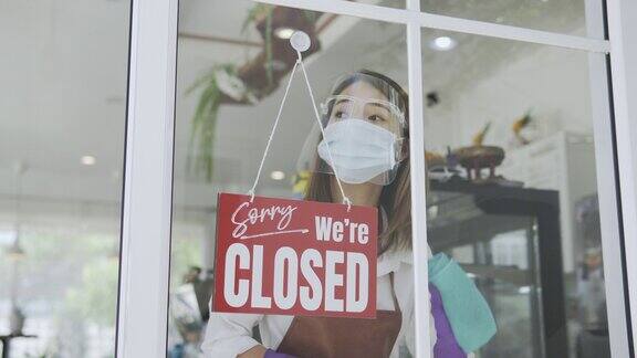 带面罩的亚洲妇女把一个标志从关闭到打开在一个门商店新冠肺炎封锁后的小型食品店生意