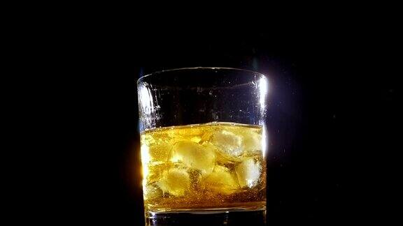 在黑色背景下冰块落入一杯威士忌的特写镜头