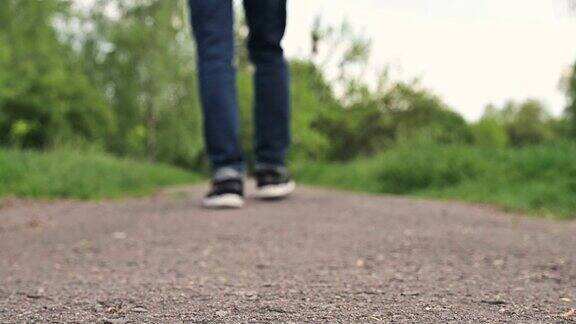 一个穿着运动鞋的男人走在一条土路上穿着牛仔裤和运动鞋的男孩正在穿过公园特写腿一个人在走