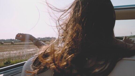 风吹着无忧无虑的年轻女子的头发开着敞篷车沿着阳光明媚的乡村田野行驶