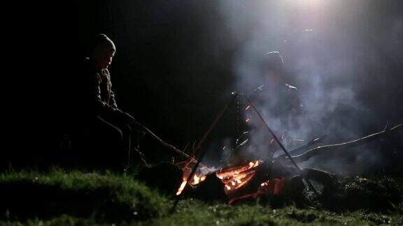 两个男孩晚上坐在篝火旁一边批改煤一边聊天