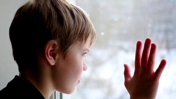 孩子坐在窗台上看着窗外的雪
