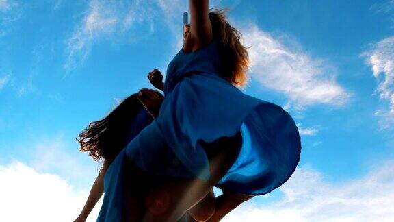两名身穿蓝色裙子的钢管女舞者在塔尖上对着天空表演舞蹈