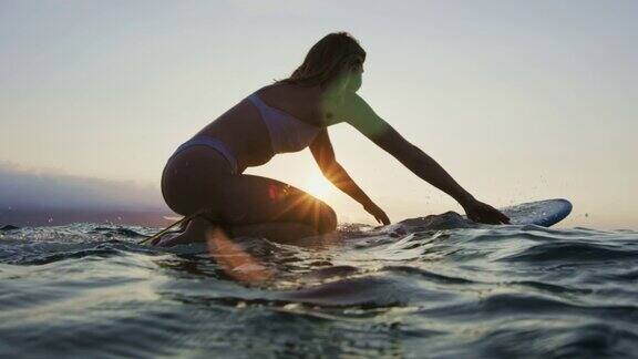 穿着比基尼在冲浪板上划水的漂亮年轻女子