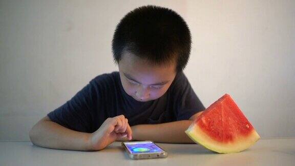 亚洲男孩坐在桌子前高兴地吃着西瓜