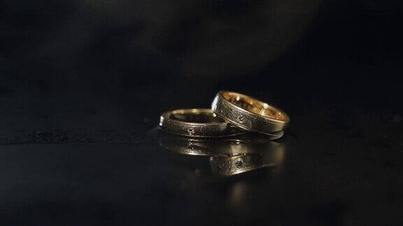 结婚戒指躺在黑暗的表面与水的反射用近距离微距发光烟慢动作