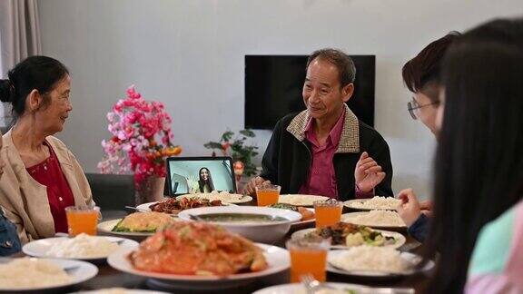 欢乐的亚洲家庭在家里吃团圆饭的时候通过数码平板电脑视频电话与亲戚们在网上欢度春节